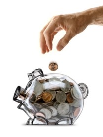 An elderly mans hand dropping a coin into a piggy bank full of coins.